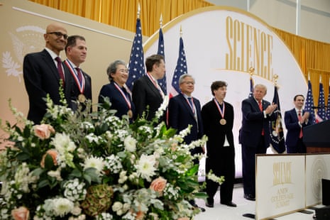 Tech CEOs wearing medals stand on stage as President Trump applauds beside them