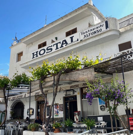 A whitewashed building labelled hostal with cafe tables and chairs and trees in front of it