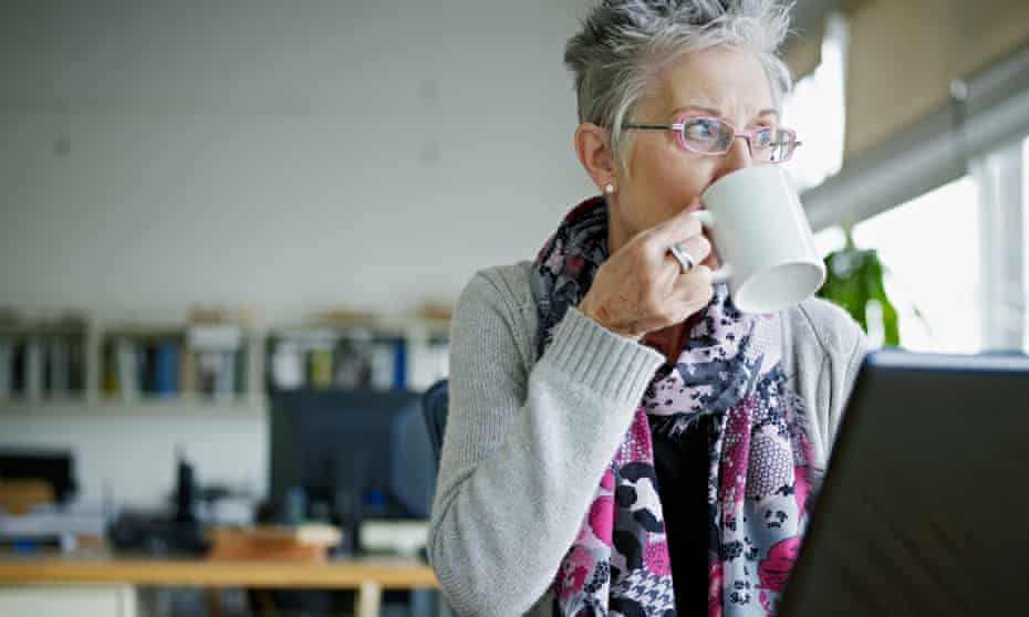 A businesswoman with grey hair sitting at a laptop drinking coffee