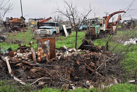 A pile of burnt-out remains in the foreground; the wrecks of agricultural machinery in the background.