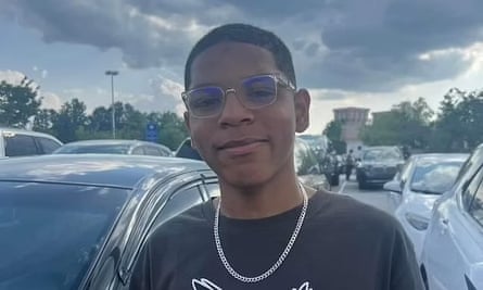 A young man smiles in front of several cars.