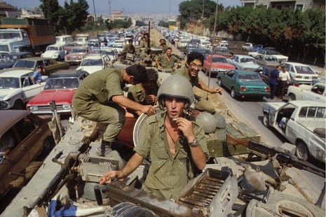 Soldiers ride atop a military vehicle down a major road