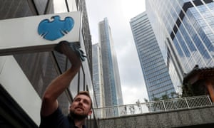 A worker cleans a Barclays logo outside a bank branch in the financial district of London