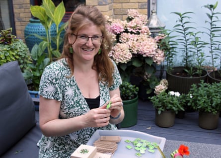 Smiling woman with glasses and long hair sitting at a table in backyard, using scissors on a project.