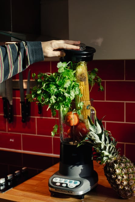 A hand presses an array of vegetables into a blender