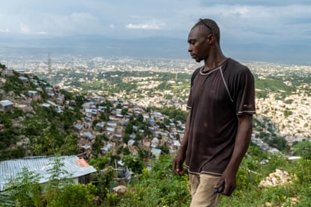 A man stands on a hillside which is covered with thousands of temporary shelters.