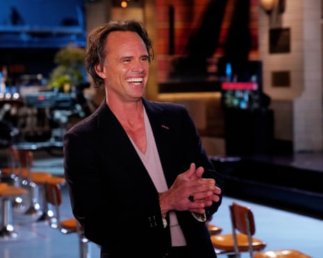 man wearing blazer smiles as he holds his hands together on stage