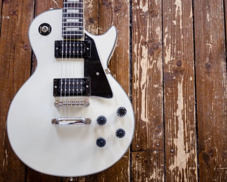 A vintage white Les Paul electric guitar lies on a distressed wooden floor