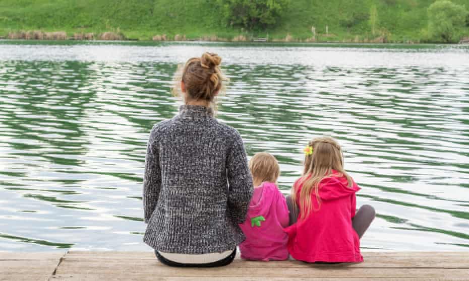 Mother with two daughters on a wooden board on the shore of lake rear view