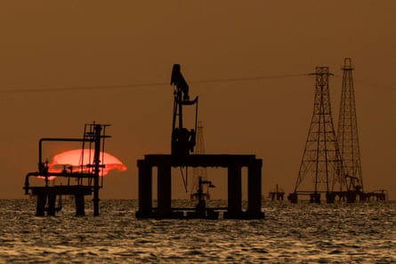 Oil platforms and pumpjacks in water, silhouetted against the sunset