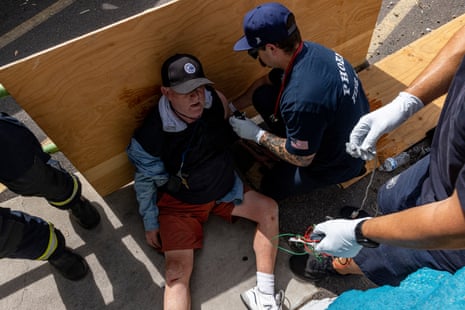 Paramedics in navy attend to a man sitting on the sidewalk with his back resting against plywood