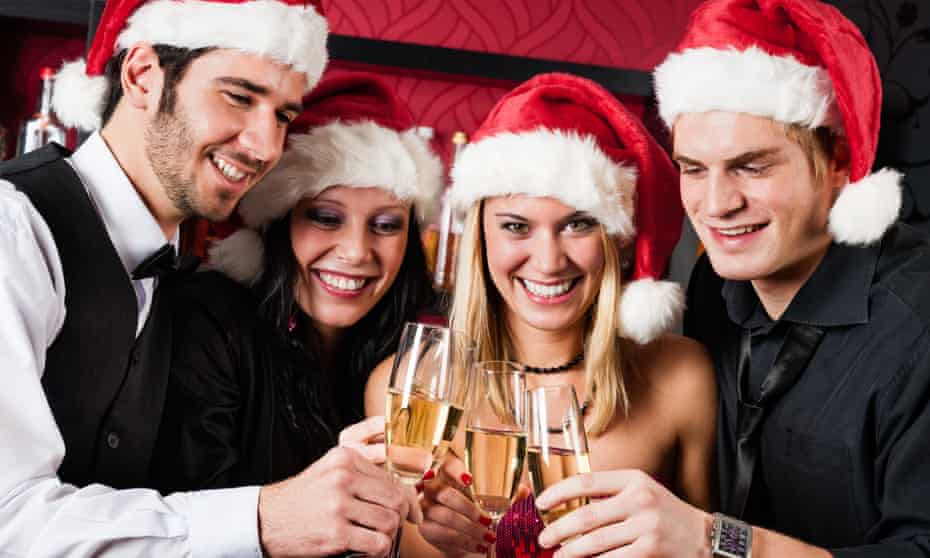 Two men and two women wearing Santa hats, grinning and toasting each other with champagne glasses