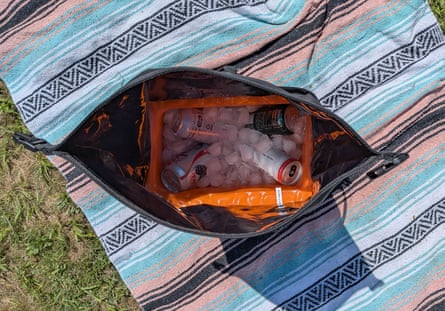 aerial view of soda cans on ice in cooler bag that’s sitting on blanket in grass