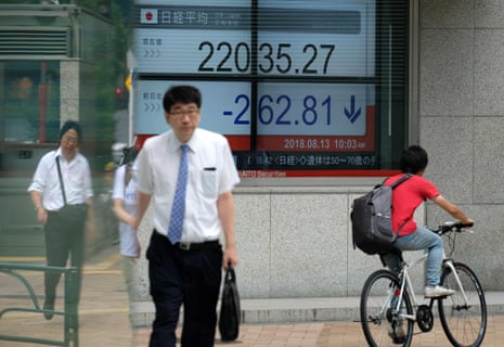 Pedestrians walking past a stock indicator showing share prices of the Tokyo Stock Exchange in Tokyo.