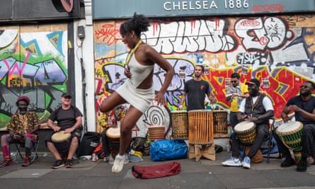 A woman jumps in the air while dancing, with drummers sitting behind her.