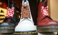 close-up of three Dr Martens boots, black, white and red, in the window of a store: they have red and white or red and green laces, and the yellow stitching on their soles can be seen clearly
