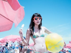 Young women in shades and a bikini poses with an ice lolly and a beach ball.