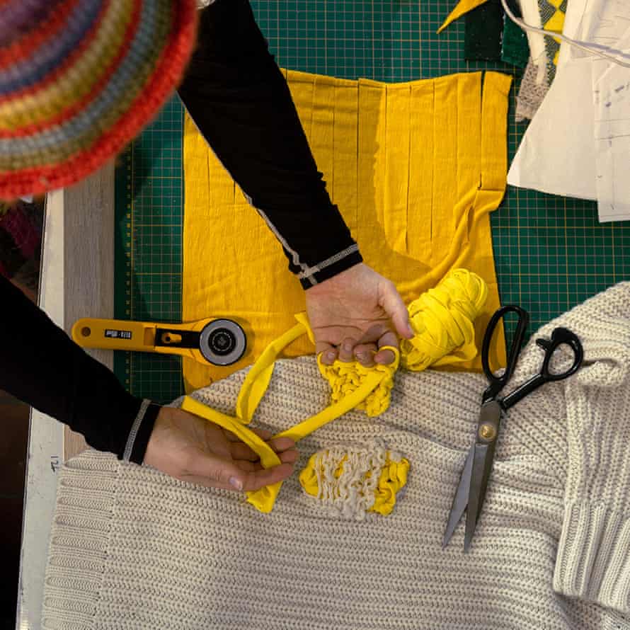 A woman's hands finger knitting yellow material, and a jumper