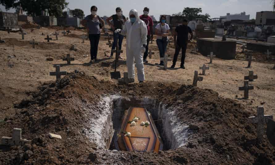 A cemetery worker stands before the coffin of a woman who is suspected to have died of Covid-19, at her burial in Rio de Janeiro.