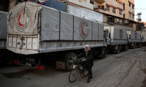 A Syrian man pushes his bicycle past a Red Crescent convoy carrying humanitarian aid in Kafr Batna on the outskirts of the capital Damascus.