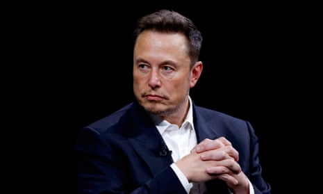 Elon Musk at a tech conference: he has his hands clasped and is photographed against a black background