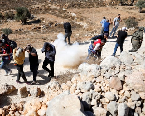 Palestinians cover their heads from a stun grenade on a gravel road
