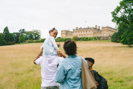 A family walks up a grassy hill towards a stately home