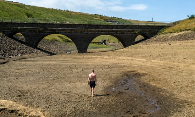 A man walks along a dry bank of a tributary to the Dowry Reservoir close to Oldham, Greater Manchester, on Monday