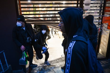 People in hoods and masks enter a ransacked Paris Franprix store through a broken shutter