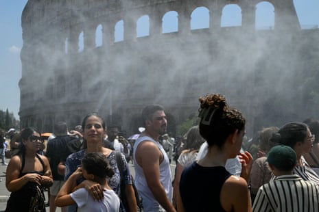 People try to cool down by standing in front of a nebuliser placed on a Civil Protection pick-up truck spraying cool water during a heatwave, in Rome near the Colosseum