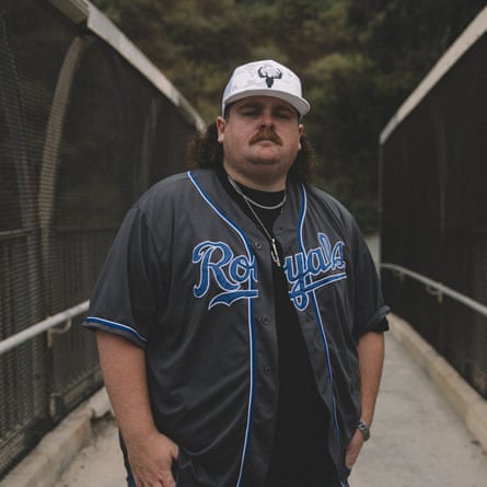 A man wearing a jersey and cap poses for a portrait on a bridge
