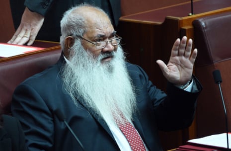 A man with a white beard and glasses raises his hand.