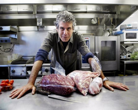 Bourdain, a chef, standing in front two slabs of meat on a silver table.