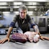 A chef standing in front two huge slabs of meat on a silver table