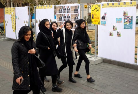 Young Iranians flash victory sign as they walk past electoral posters in Tehran