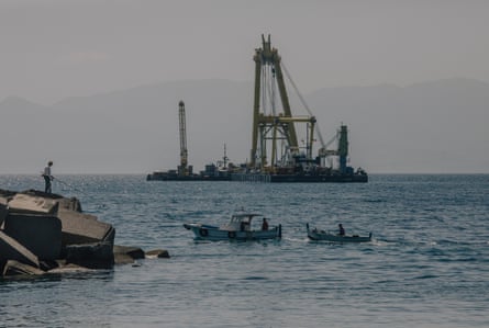 A floating crane on the sea and fishers in boats.