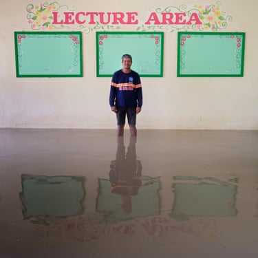 A man stands shin-deep in flood water next to a wall with the words ‘lecture area’ written on it