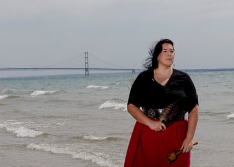 woman standing on a lake shore with a bridge behind her