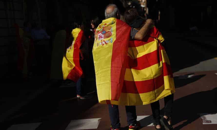 A man draped in a Spanish flag walks with a woman draped in a Catalan flag on their way to the rally.