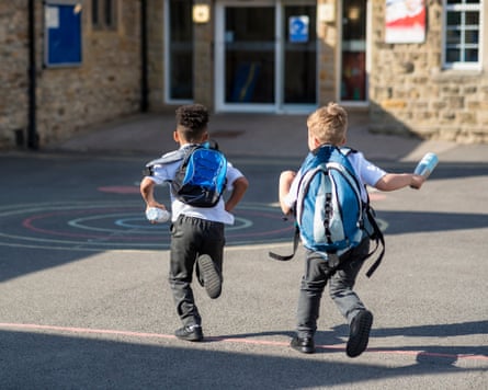 back view of two boys running in their school yard towards the door with their backpacks on.