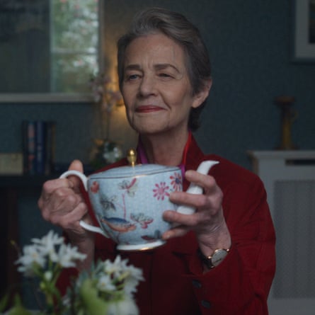 Sitting at a dinner table, she is holding an ornate china teapot in both hands and smiling weakly
