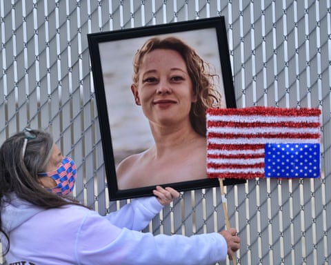 Framed photo of smiling woman next to upside-down US flag, held by woman in Covid mask covered with US flags.