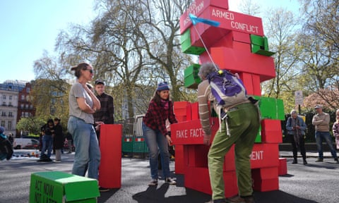 Jovens empilham-se em uma escultura colorida, com blocos com slogans como "fatos falsos" e "conflito armado".
