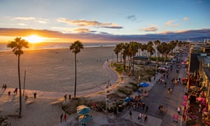 Tourists walking on footpath by beach during sunset. High angle view of Venice beach during sunset.