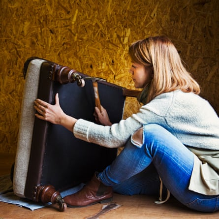 An upholsterer working on the underside of a chair seat in an upholstery workshop.