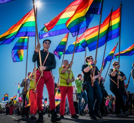 A crowd of people holding rainbow flags in the sun
