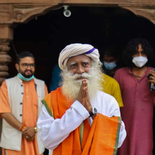 An older man in a saffron robe giving a namaste greeting 
