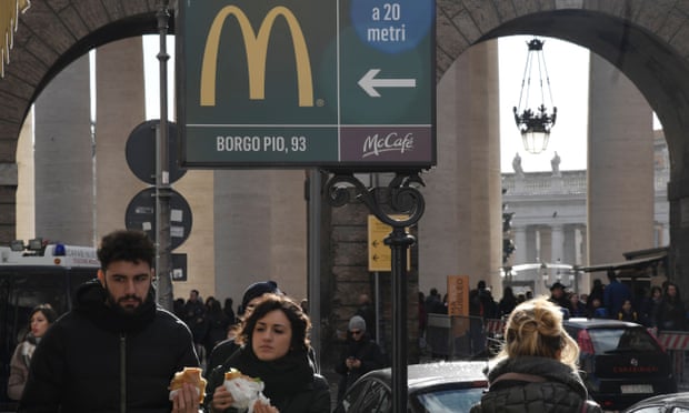 A sign pointing the way to a McDonald’s restaurant with St Peter’s Square in the background
