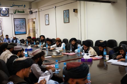 A class of Taliban members sit around a large table with pens and worksheets