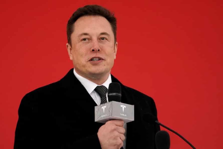 Elon Musk hält ein Mikrofon mit einem Tesla-Logo darauf.
